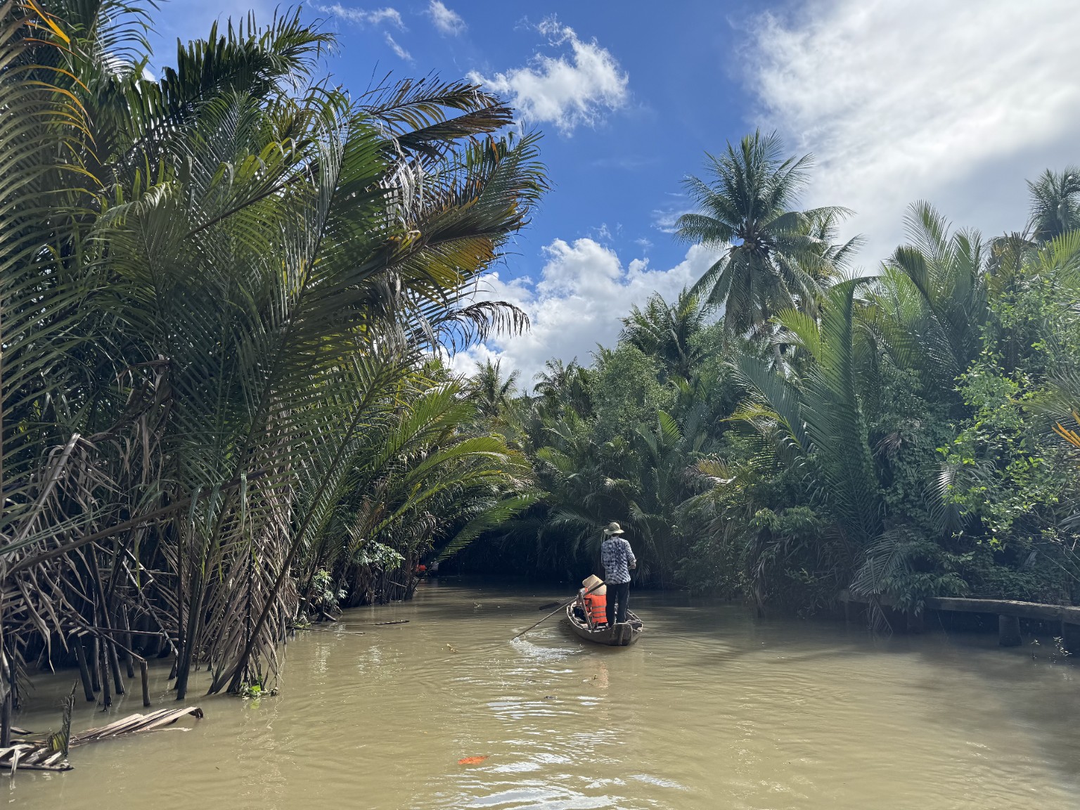 A traditional hand-rowed sampan travelling through a narrow nipa-palm canal in Ben Tre