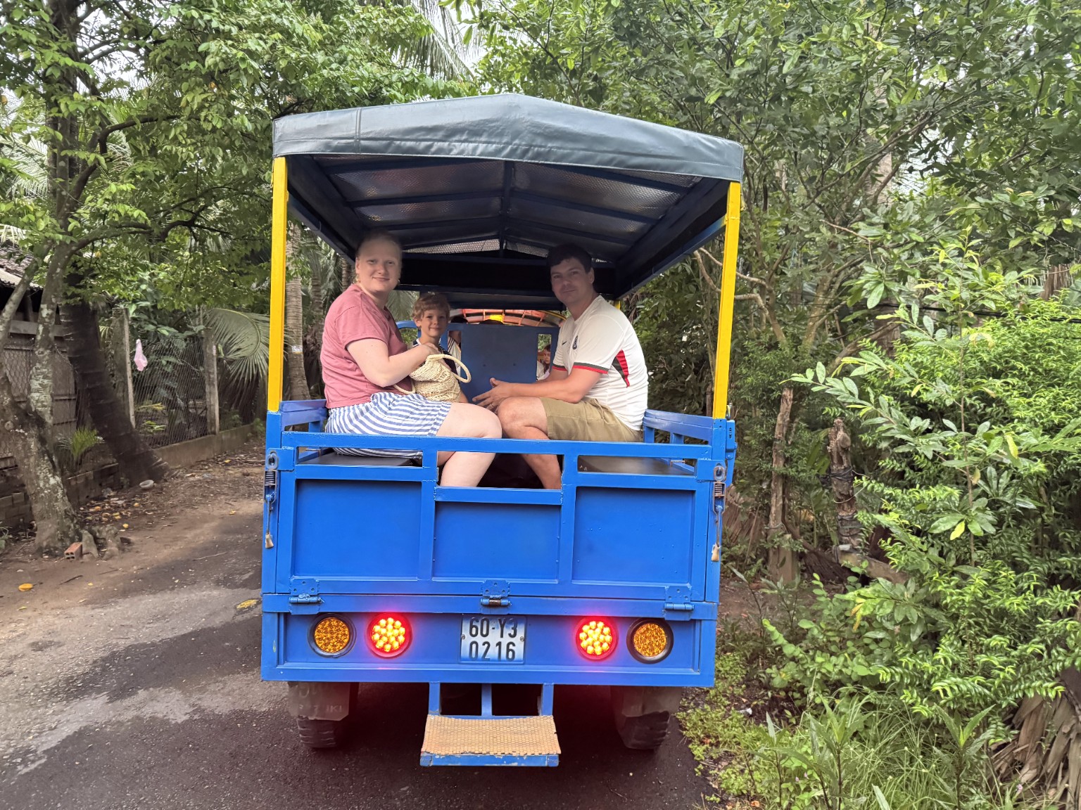 A family riding a local tuk-tuk on a green village road in Ben Tre