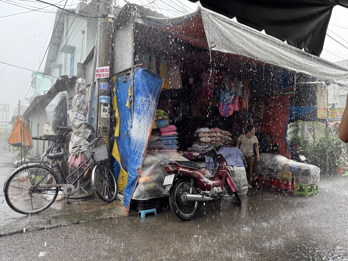 Heavy rain falling beside a covered village market stall in Mỹ Lồng