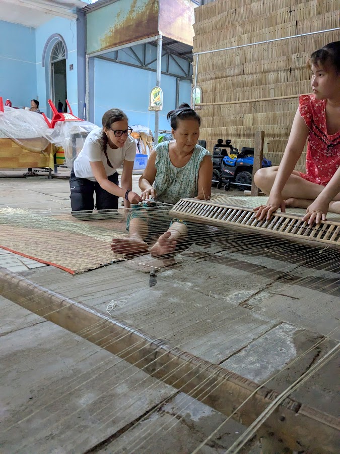 A solo traveler learning mat weaving with two local women