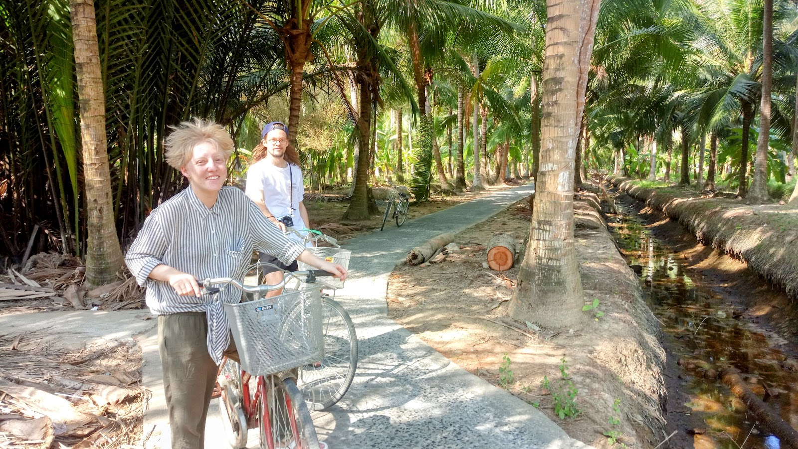 Guests cycling beside a garden canal under coconut palms