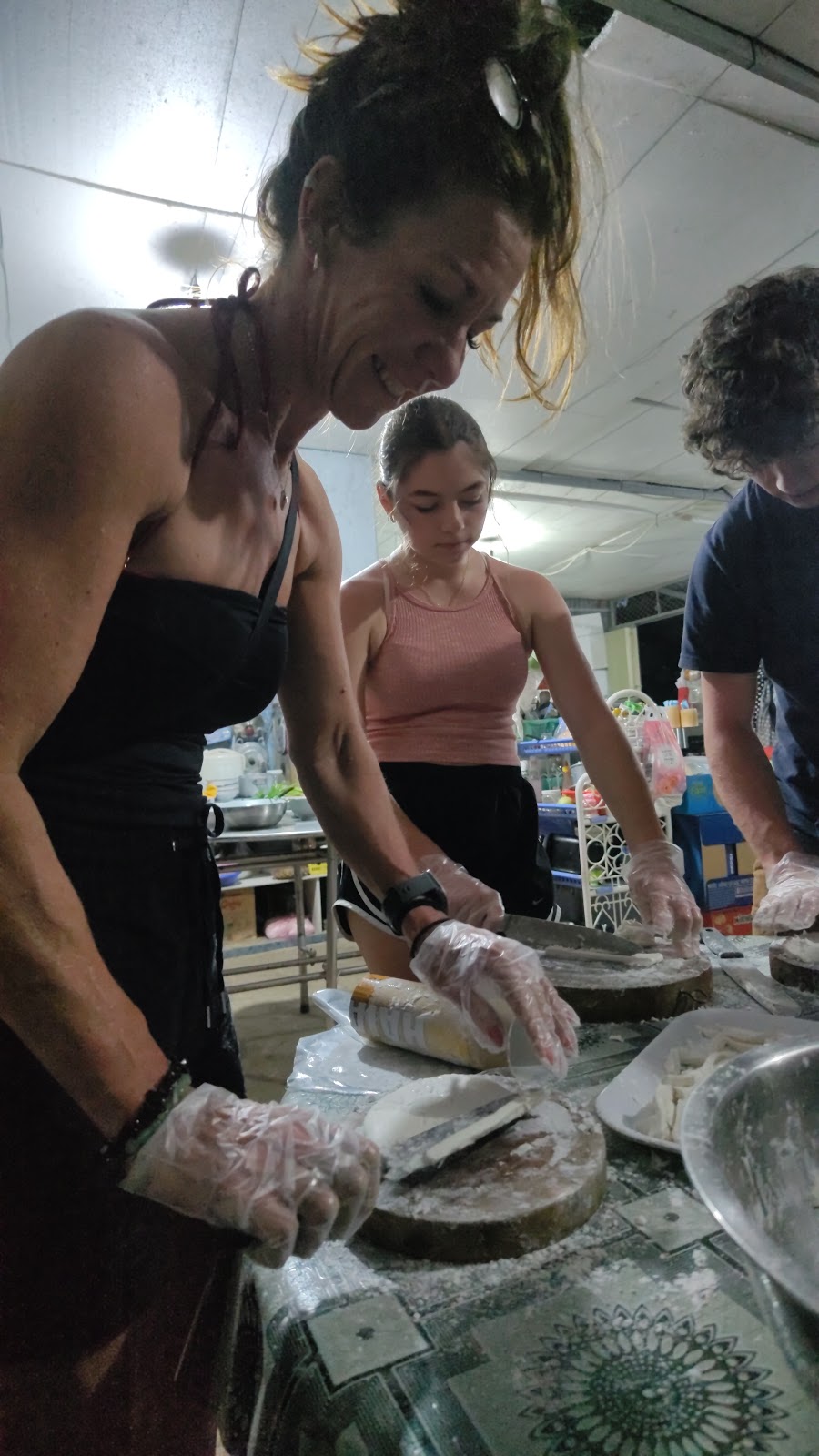 Guests wearing gloves and cutting rounds of dough into bánh canh bột xắt noodles during a cooking class