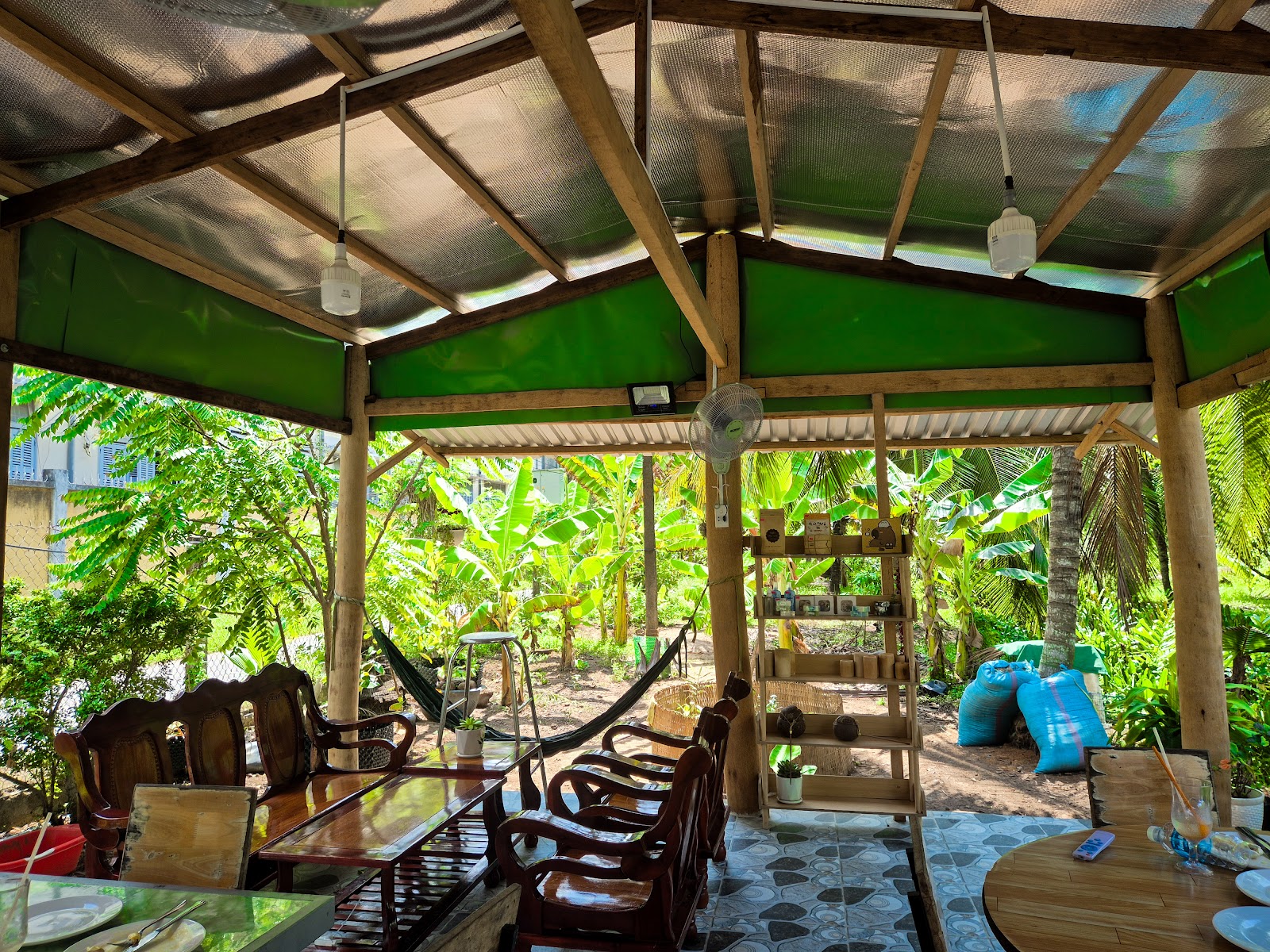 Open-sided wooden seating area with tables and hammocks looking into the tropical garden at Thúy Café in Ben Tre