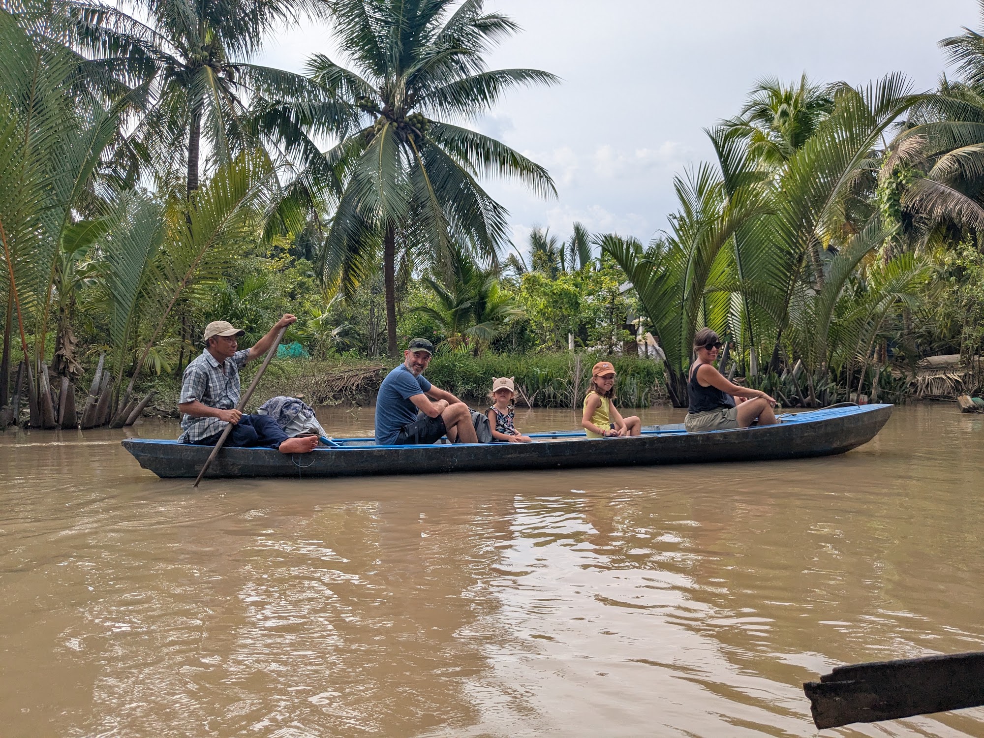 Travelers riding a traditional hand-rowed sampan through a coconut canal in Ben Tre