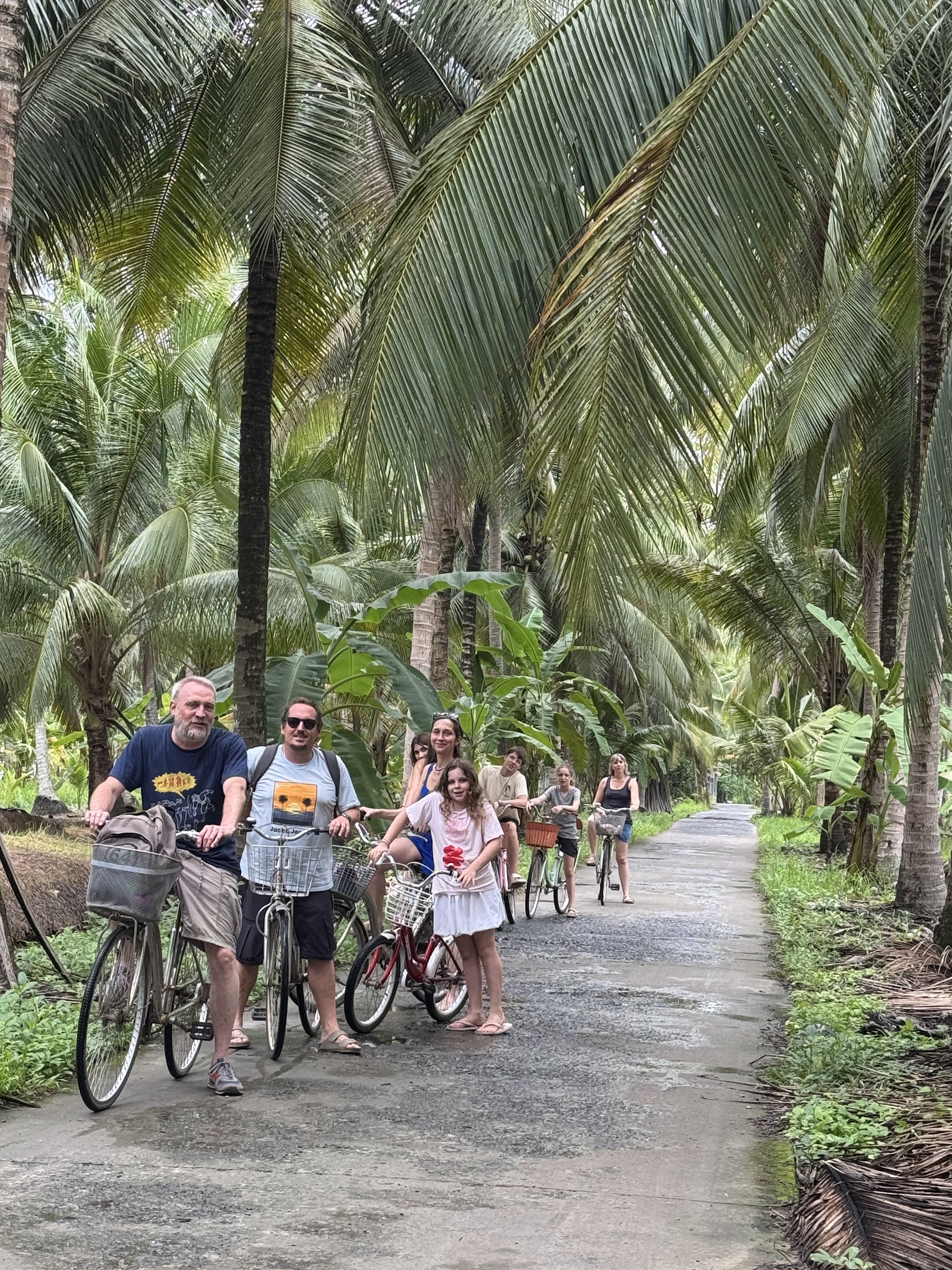 A small international group cycling on a coconut-shaded lane in Ben Tre