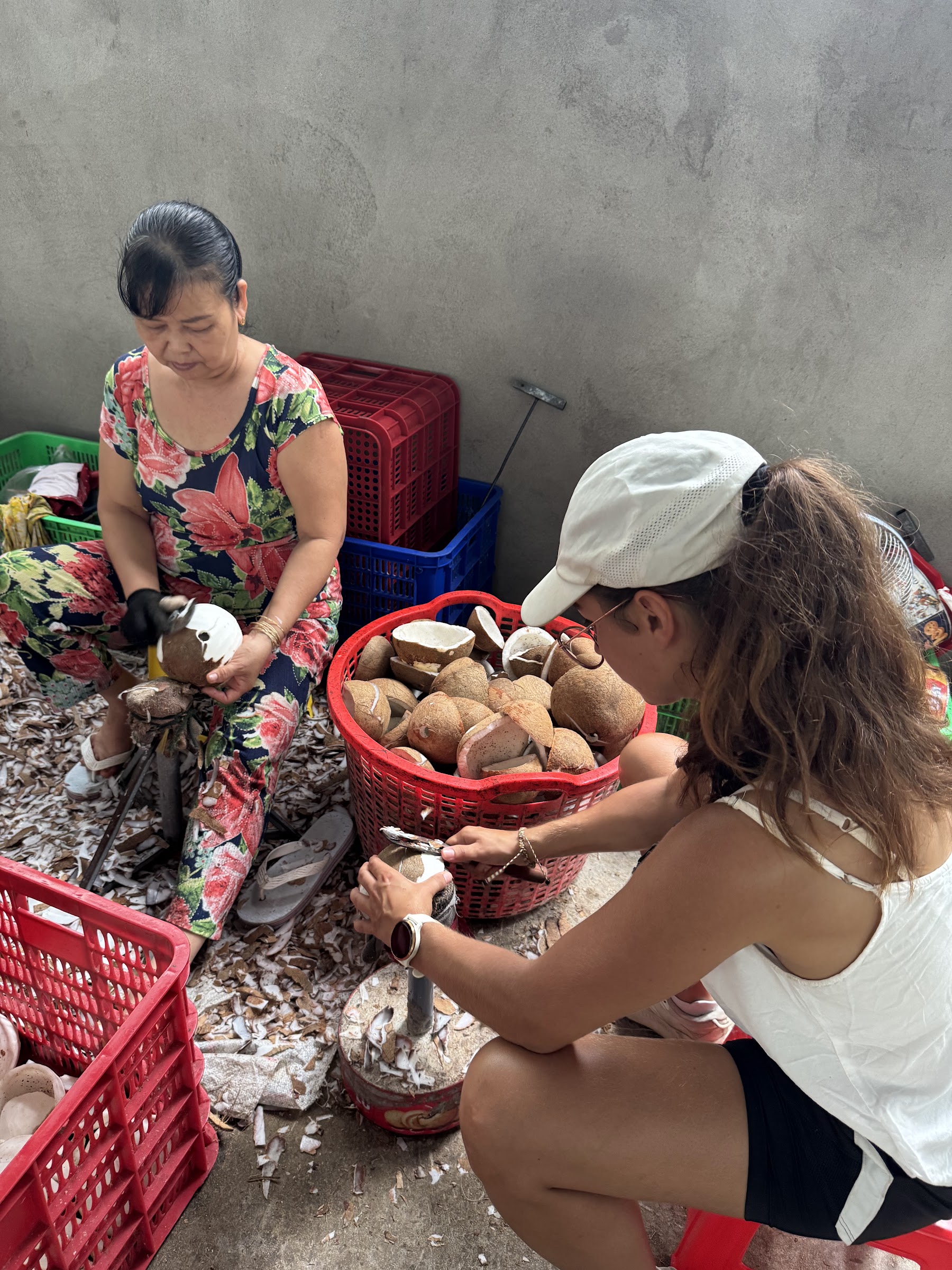 A visitor learning coconut preparation beside a local worker in Ben Tre