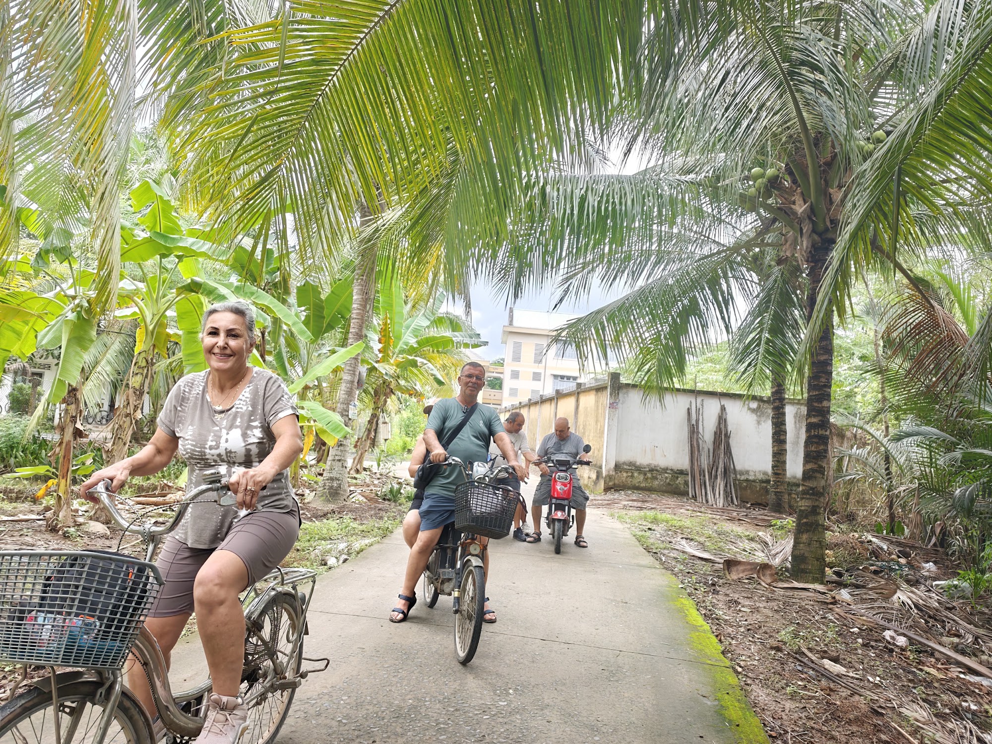 Travelers cycling with a local host on a narrow village lane in Ben Tre