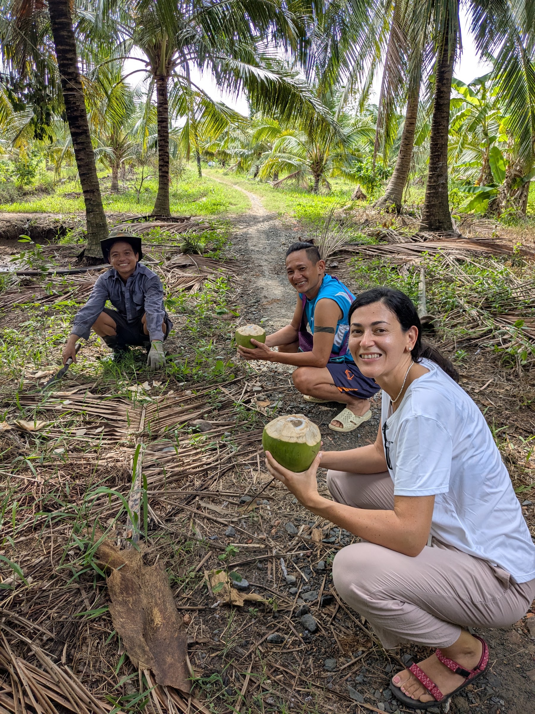 A guest drinking fresh coconut with Thuần and local family members in a Ben Tre garden